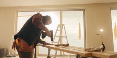 Person using a drill on a wooden plank indoors.