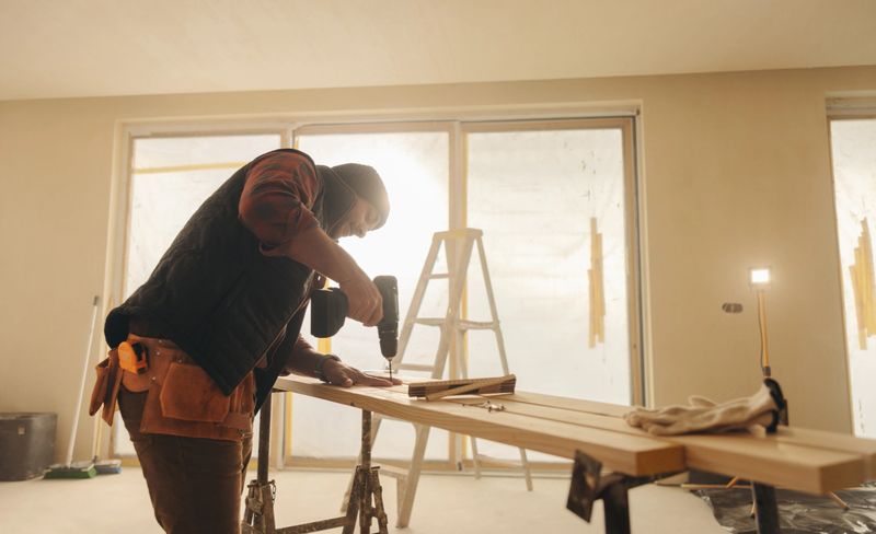 General contractor renovating a kitchen in a home. Construction worker using a power drill n on wood planks for baseboard installation. A skilled worker and tools ensure a successful interior remodel.