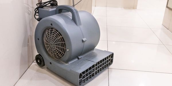 A gray industrial air blower on white tiled floor.