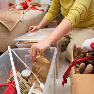 Person organizing holiday decorations into plastic bins and boxes.