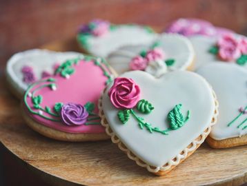 Heart-shaped cookies with floral icing decorations on a wooden platter.