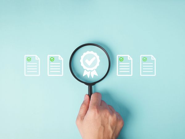 Hand holding magnifying glass over
certification icons symbolising compliance and quality assurance