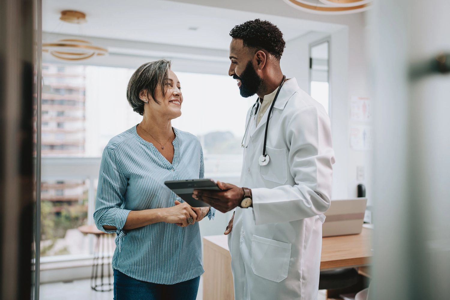 A doctor and patient smiling during a consultation in a bright office.
