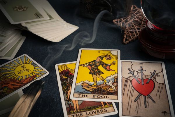 Tarot cards, incense smoke, and a crystal ball on a dark surface.