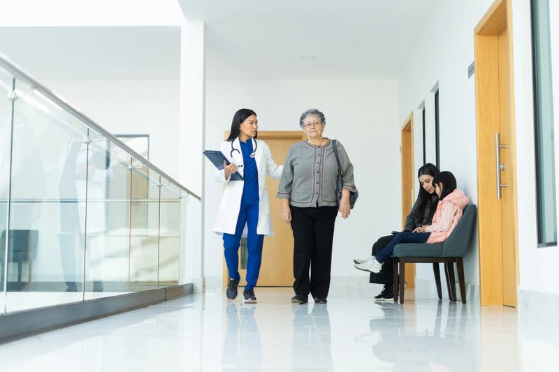 The doctor offers gentle guidance, walking alongside the elderly patient to the exam room, ensuring a comforting transition into the medical checkup process.