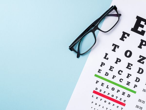 Eye chart and black eyeglasses on a light blue surface.