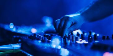 A DJ adjusts controls on a mixer under blue lighting.