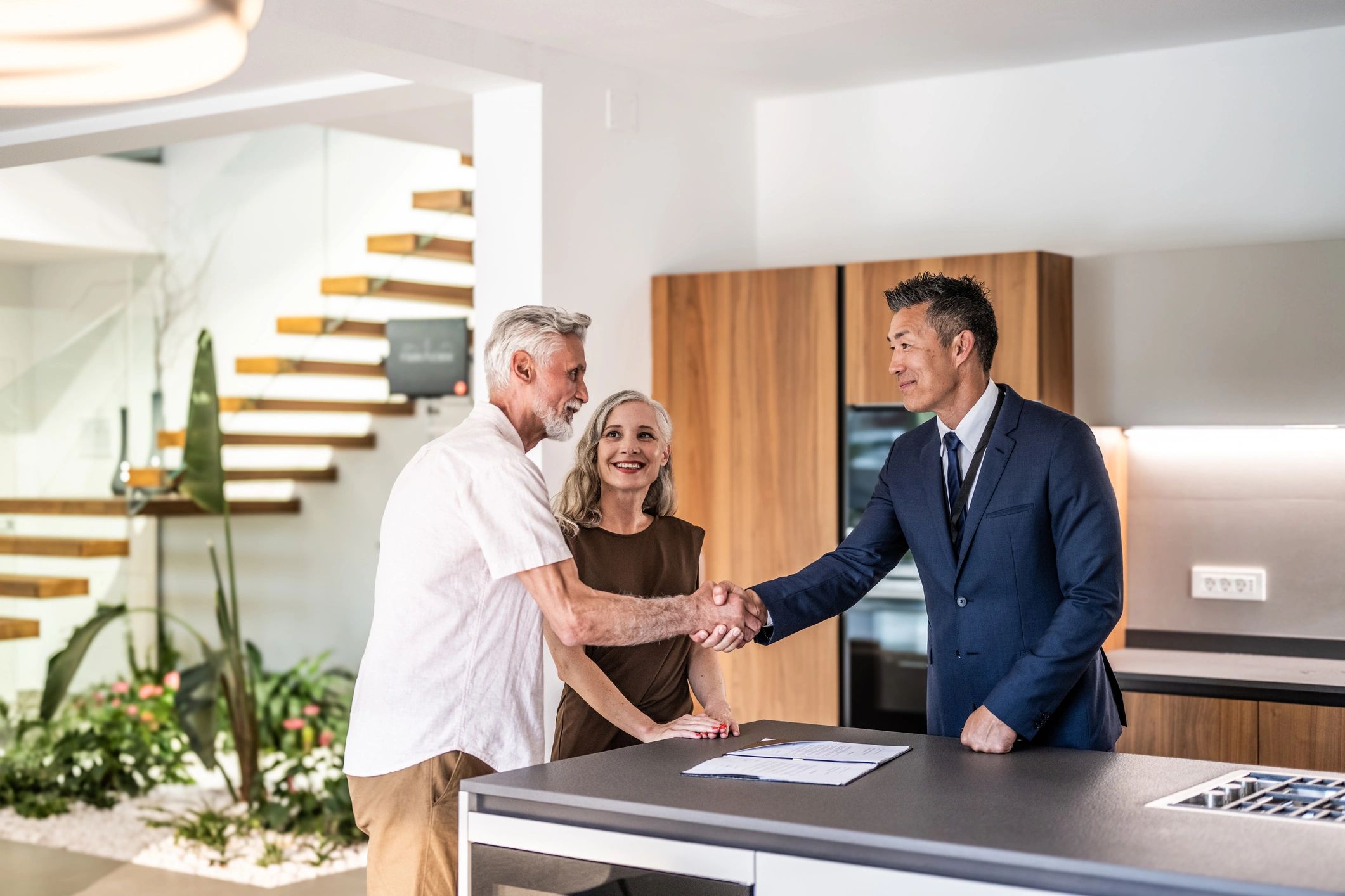 Couple shakes hands with a real estate agent in a modern home.