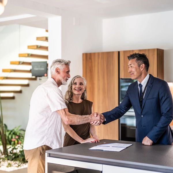 Real estate agent shakes hands with elderly couple in modern home.