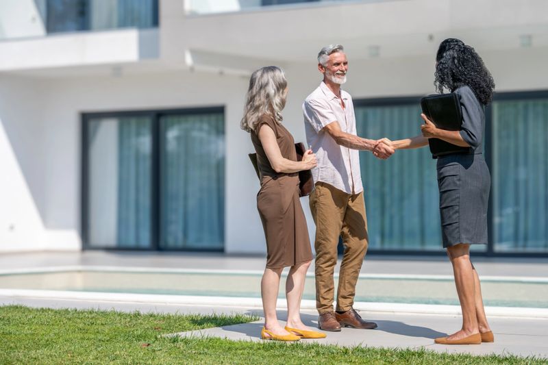 Female real estate agent showing luxury house to senior couple and shaking hands wide shot