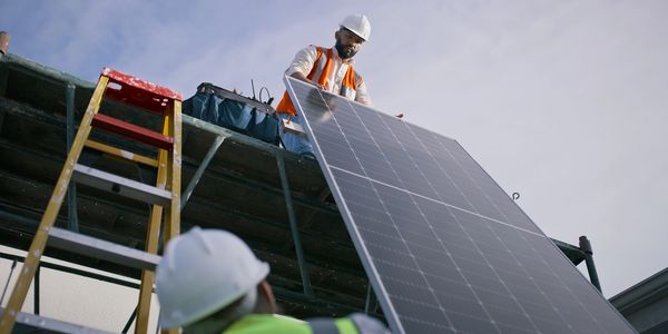 Workers installing a large solar panel on a rooftop.