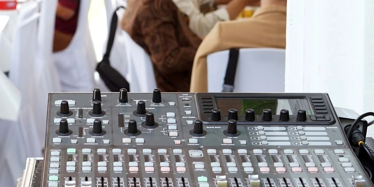 A professional audio mixing console with knobs and sliders in a live event setting.