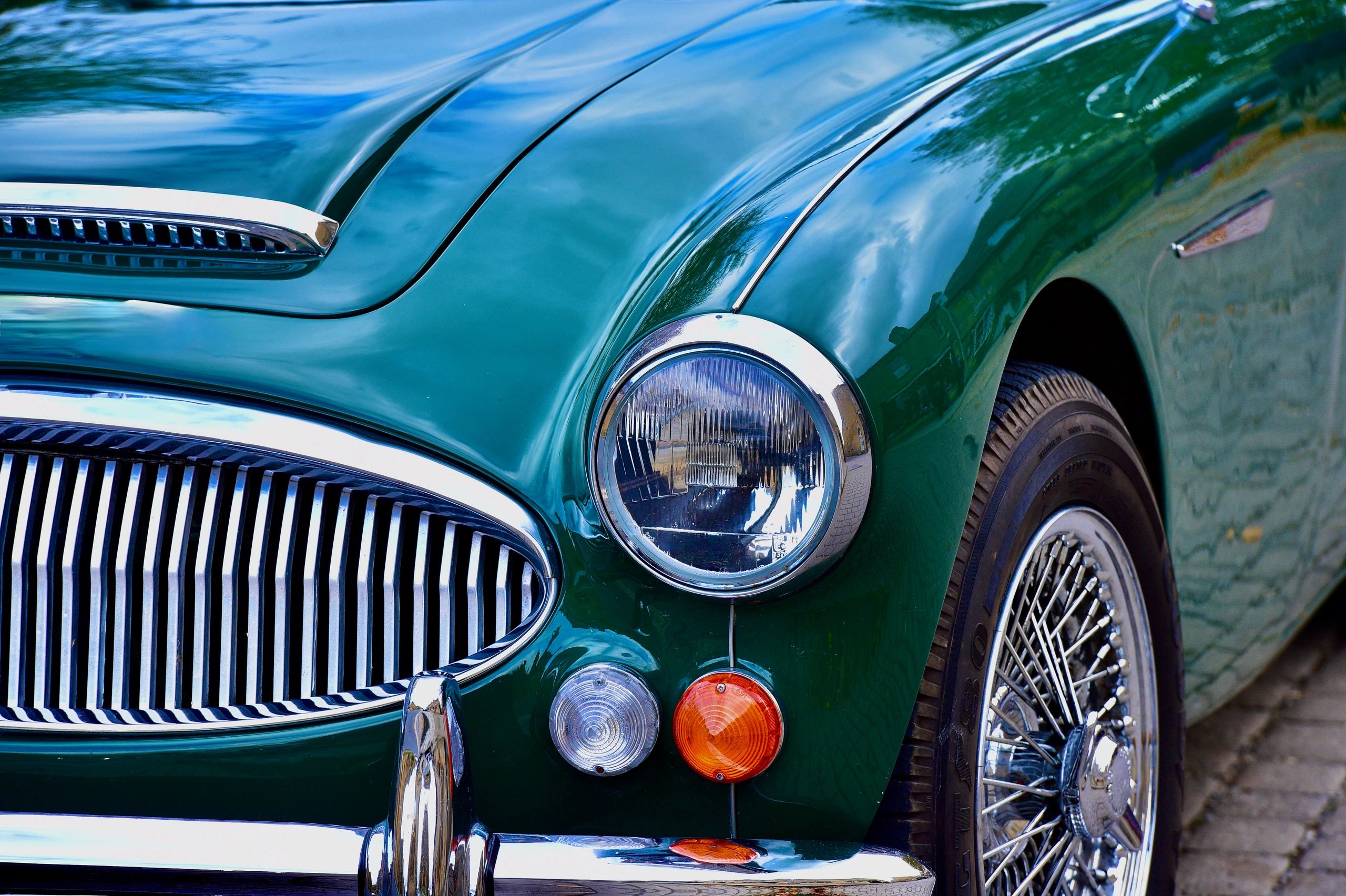 Close-up of a vintage green car's front headlight and grille with chrome detailing.