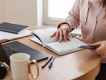 generic image of a female, at a desk writing notes and with a laptop open. 