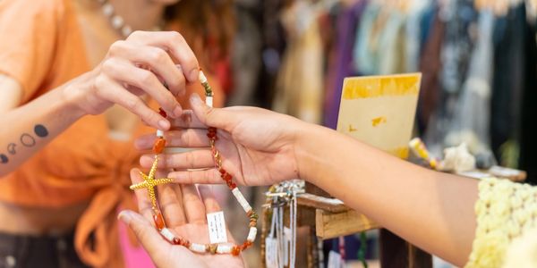 Two people exchanging a beaded necklace with a starfish pendant at a market.