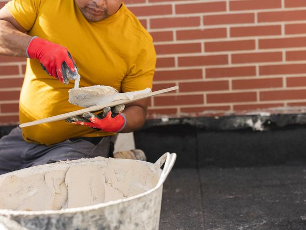 Worker wearing red gloves applying plaster on a trowel near a brick wall.