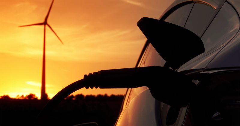 Close-up of electric car being charged with plug-in power cord at charging station during sunset.