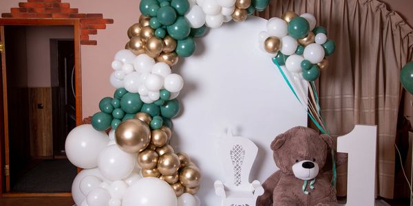 First birthday party setup with balloons, teddy bear, and decorative chair.