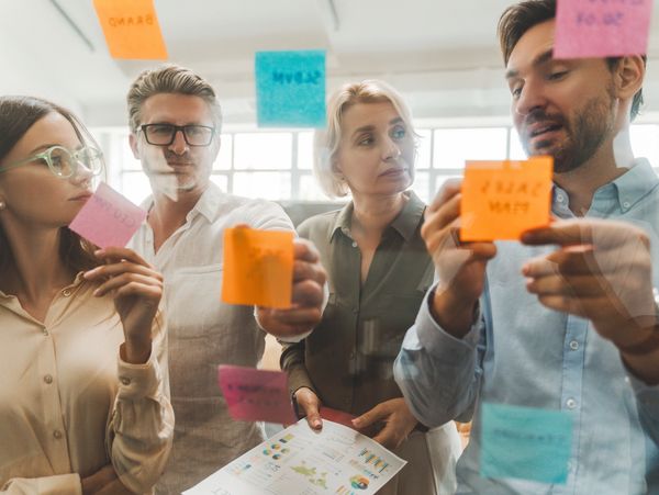Four colleagues brainstorming with colorful sticky notes on a glass wall.