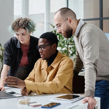 Three colleagues collaborating and discussing work on a laptop in a modern office.