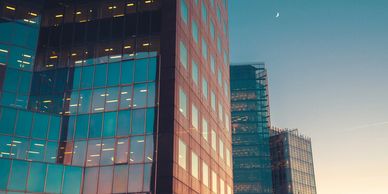 Modern glass skyscrapers reflecting the sunset and a crescent moon in the sky.