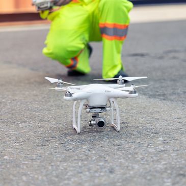 A white quadcopter drone on the ground with a person in neon workwear.
