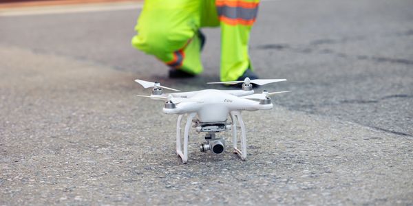 White drone on the ground with a person in safety gear in the background.