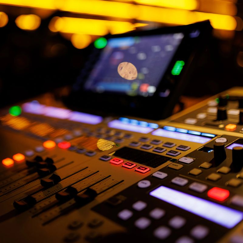 Modern sound mixer console with colorful buttons and sliders, set against the backdrop of a live music venue.