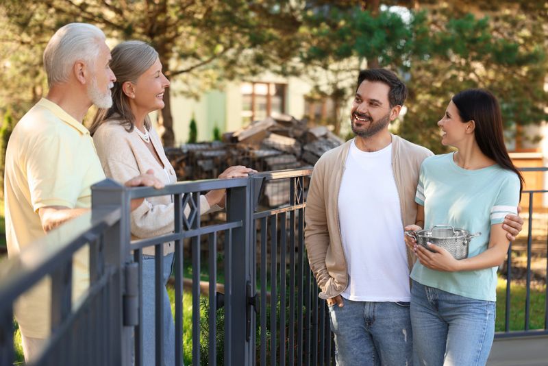 Friendly relationship with neighbours. Young family talking to elderly couple near fence outdoors