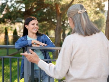 Two women happily talking outside by a fence.