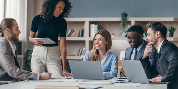 Group of smiling business professionals collaborating at a desk with laptops