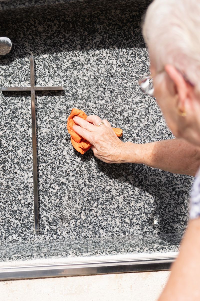 view over the shoulder of an old widow woman cleaning a grave in the cemetery.maintenance of the family gravestone.vertical image.