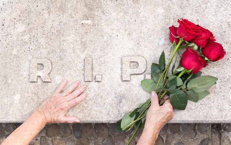 point of view of an elderly widowed woman caressing the stone and placing flowers on the grave at a family funeral.burial and ceremony in a cemetery.
