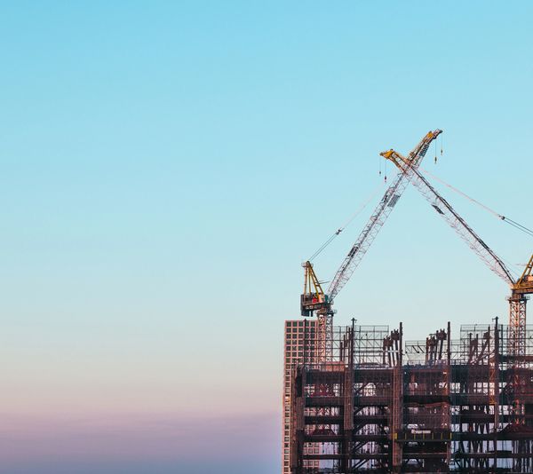 Two cranes working on a high-rise building under construction at sunset.