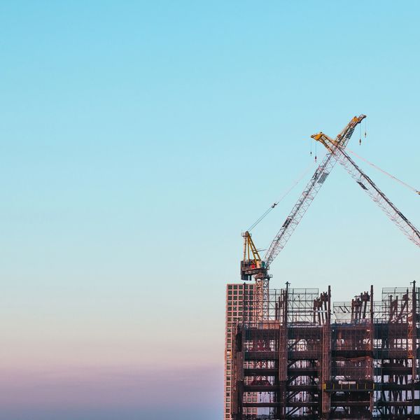 Two cranes working on a building construction site against a clear sky.