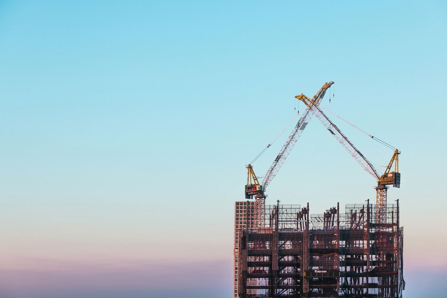 Two construction cranes forming an X over a building under construction at sunset.