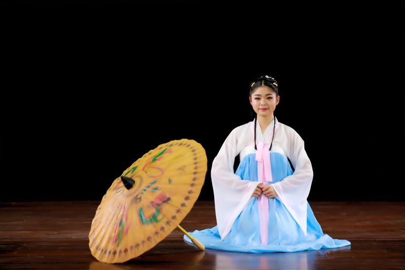 A young woman in a Chinese traditional dress sits with an umbrella in the studio. Chinese New Year