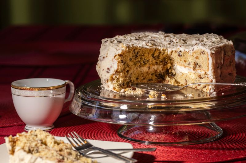 Buttercream Pecan cake on aglass stand set on a table with red linen with porcelain plate and coffee cup