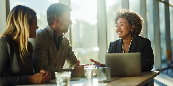 Business meeting with three professionals discussing at a table near large windows.