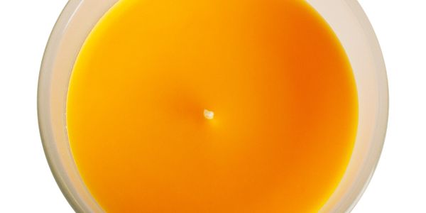 Top view of a lit yellow-orange candle in a glass container.