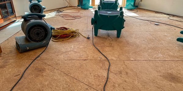 Air movers and extension cords on a bare floor inside a room.