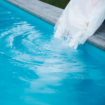 A person pouring a substance into a swimming pool.