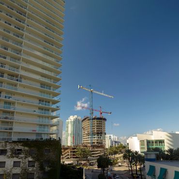 Construction cranes towering over a cityscape with modern buildings under a clear blue sky.