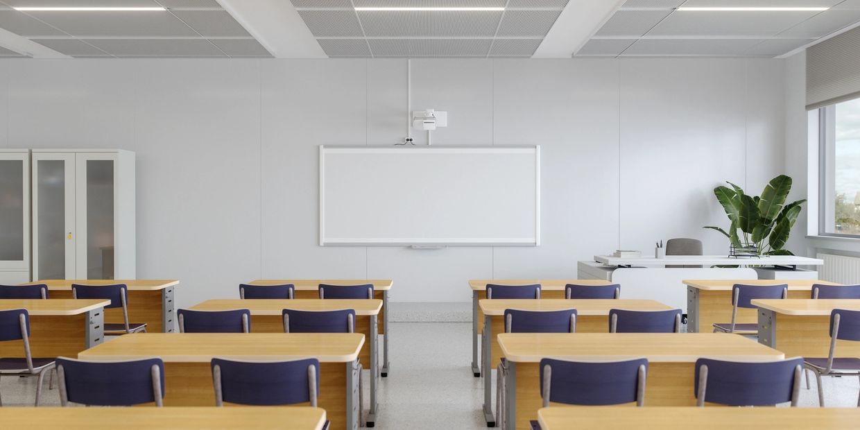 Empty classroom with wooden desks and blue chairs facing a whiteboard.