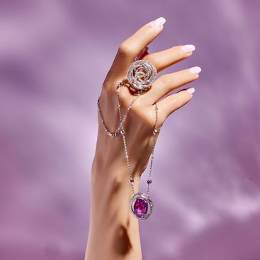 Elegant hand adorned with a sparkling diamond ring and a delicate silver chain with a purple gemstone pendant.