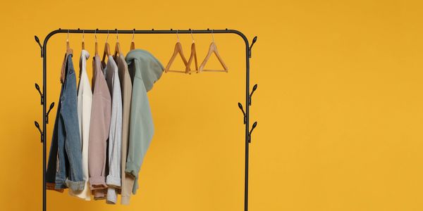 Clothing rack with hoodies and jackets against a yellow background.