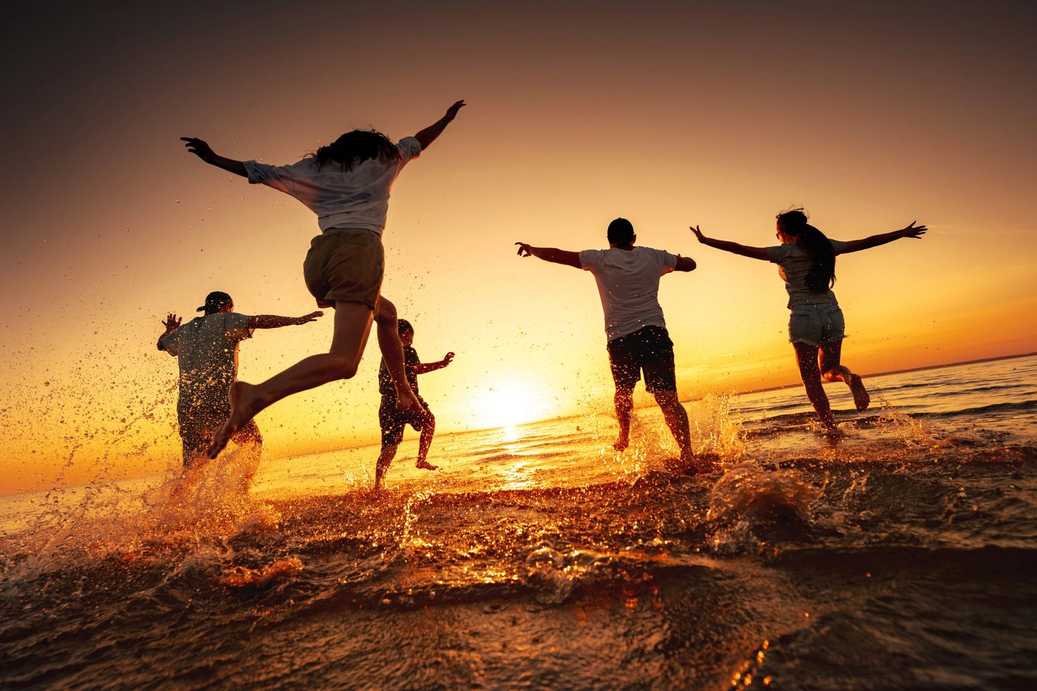 Friends joyfully jumping and splashing in the ocean at sunset.
