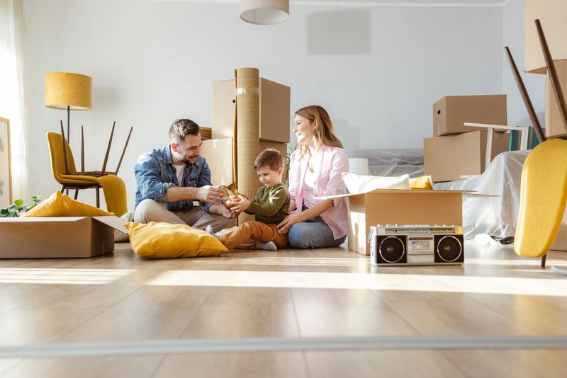 Happy family with one child starting new life in new apartment. They are unpacking boxes and talking to the child while sitting on the floor