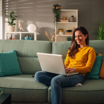 Woman sitting on couch using laptop, smiling.