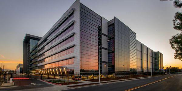 Modern glass building reflecting a colorful sunset sky at dusk.